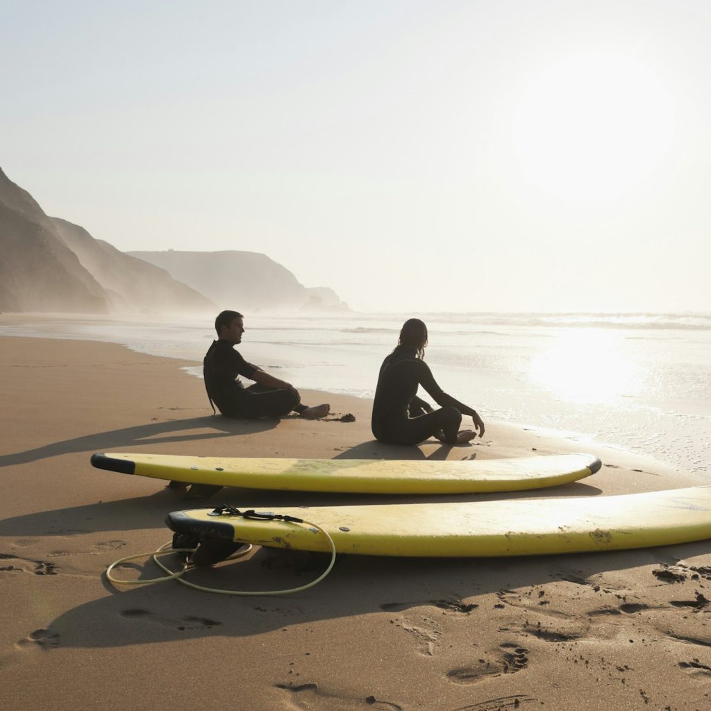 Portugal, Couple sitting on beach by surfboard